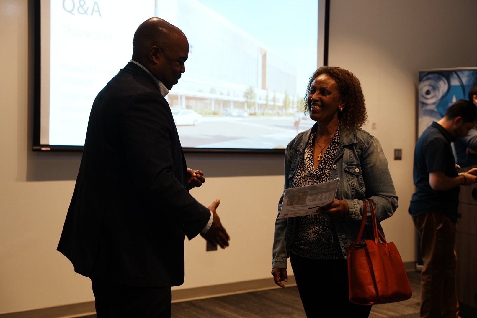 A project representative speaks with an attendee in front of the hospital rendering